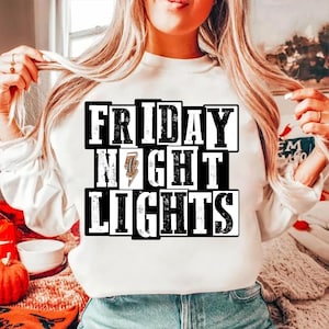 May include: White sweatshirt with the text "FRIDAY NIGHT LIGHTS" in a black and white block design. The word "NIGHT" features a lightning bolt graphic. The sweatshirt is a casual style.
