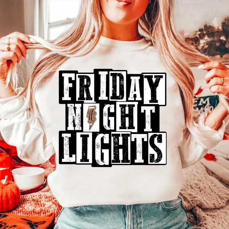 May include: White sweatshirt with the text "FRIDAY NIGHT LIGHTS" in a black and white block design. The word "NIGHT" features a lightning bolt graphic. The sweatshirt is a casual style.
