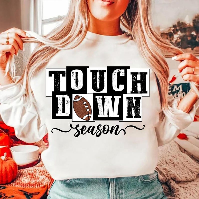 May include: White sweatshirt with the words "TOUCH DOWN" in a black and white block design, with a brown football in the center. The word "season" is written in a cursive font below the text.
