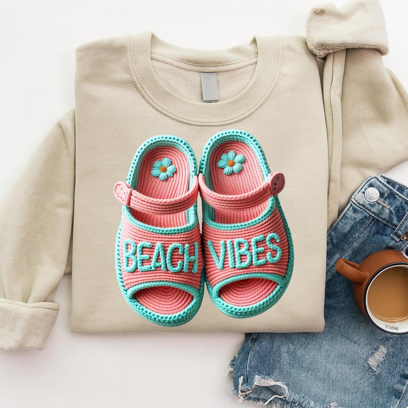 Może przedstawiać: Beżowa bluza z parą r&oacute;żowo-turkusowych sandał&oacute;w zrobionych na szydełku. Na sandałach napis "BEACH VIBES". Każdy sandał ma mały turkusowy kwiat.