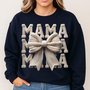 May include: Navy blue sweatshirt with the word "MAMA" in a textured, off-white font. A large, textured bow in the same off-white color is centered on the sweatshirt. The design has a 3D effect, creating a visually appealing and stylish look.