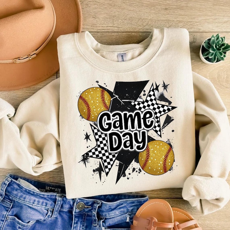 May include: A cream-colored sweatshirt with a black and white checkered star design, two yellow softball graphics, and the text "Game Day".