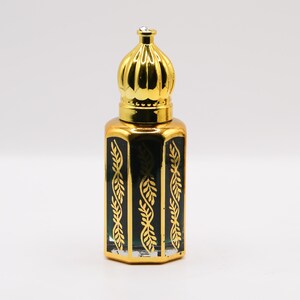 May include: A decorative perfume bottle with a gold-colored crown-shaped lid and a rectangular body. The bottle is dark green with gold leaf-like patterns. A small, clear gem is set on the top of the lid. The bottle is likely made of glass.