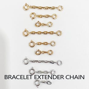 Pode incluir: Uma coleção de correntes extensoras para pulseiras em metal dourado e prateado de vários comprimentos, cada uma com um fecho de mola circular numa extremidade e um anel na outra. O texto BRACELET EXTENDER CHAIN é visível na parte inferior.