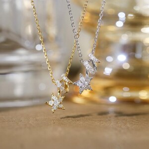 May include: Two delicate necklaces featuring star-shaped pendants encrusted with small clear stones. One necklace is crafted from yellow gold-toned metal, while the other is made of silver-toned metal, both featuring fine link chains and star charms.