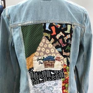 May include: Pale blue denim jacket with a patchwork design on the back. The patchwork features various fabric patterns, including floral, polka dots, and a section with the text "Fresh Pies".