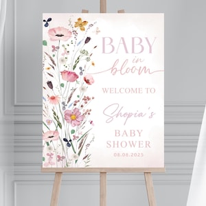 May include: A baby shower welcome sign on an easel. The sign features the text "BABY in bloom" and "Welcome to Shopia's BABY SHOWER 08.08.2025" in pink script. Floral watercolor art decorates the left side of the sign.