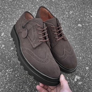Può includere: Scarpe brogue in pelle scamosciata marrone con una spessa suola in gomma nera. Le scarpe hanno una chiusura con lacci e un design a punta alare.
