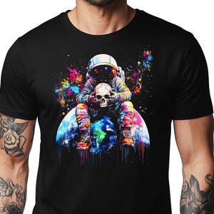 May include: Black t-shirt featuring a colorful graphic of an astronaut holding a skull while sitting on a vibrant depiction of Earth. The astronaut is wearing a helmet and colorful space suit. The artwork includes splashes of color.