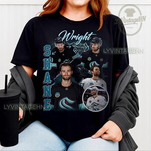 May include: Black t-shirt featuring a collage of hockey player Shane Wright. The design includes the name "Wright" in cursive and the name "SHANE" vertically. The shirt has a vintage logo in the upper right corner.