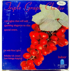 May include: A blue box with a cluster of red grape lights and a green leaf. The text says "Triple Grape Cluster" and "144 Lights that will add sparkling elegance to that special event."