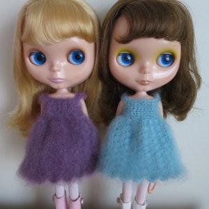 Può includere: Due bambole con occhi blu e capelli lunghi che indossano abiti viola e blu con stivali rosa e bianchi.