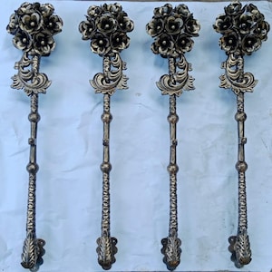May include: Four ornate, bronze-colored metal door handles. Each handle features a floral bouquet at the top, decorative scrollwork, and a textured stem. The handles are designed with a vintage aesthetic.
