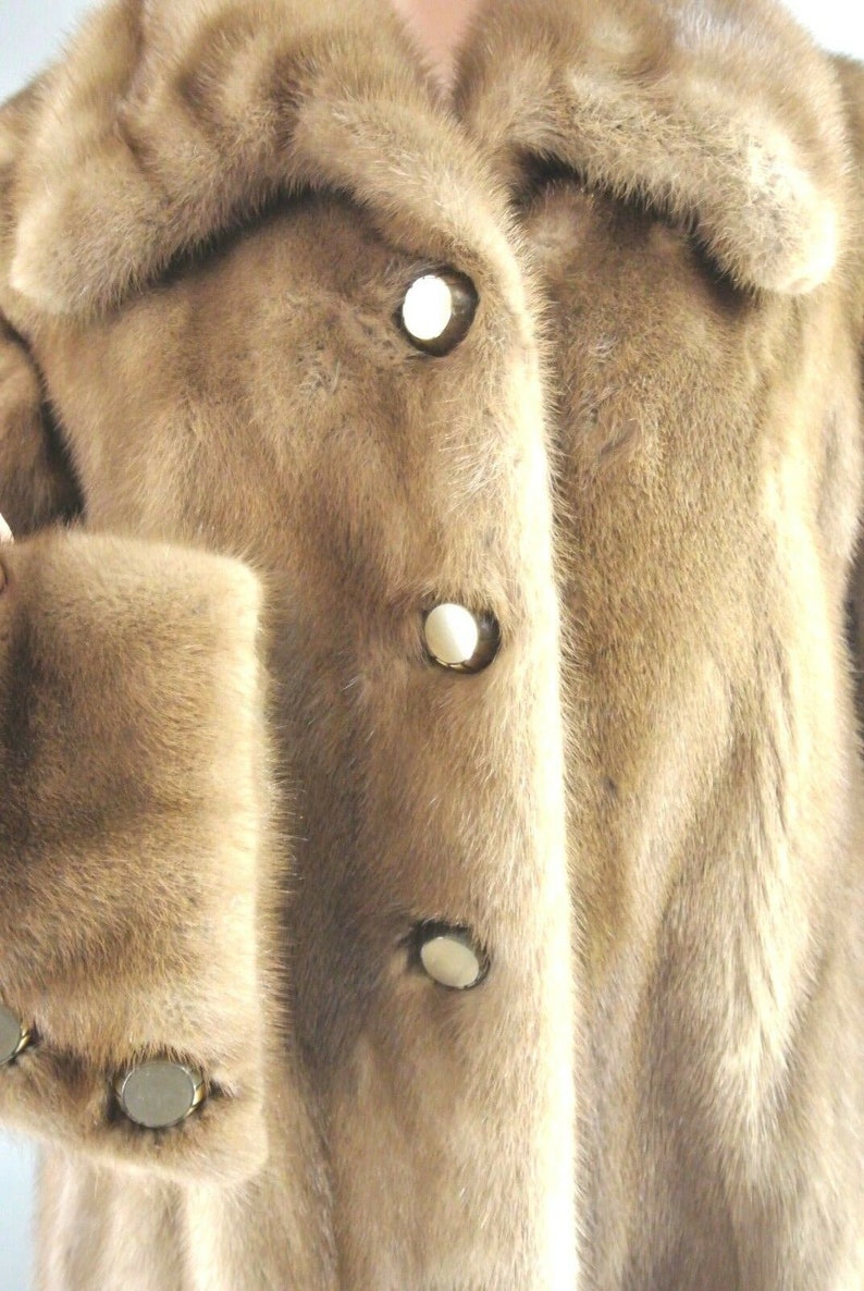 K&ouml;nnte beinhalten: Ein brauner Pelzmantel mit einem gro&szlig;en Kragen und vier goldenen Kn&ouml;pfen. Der Mantel ist aus weichem, luxuri&ouml;sem Pelz gefertigt.