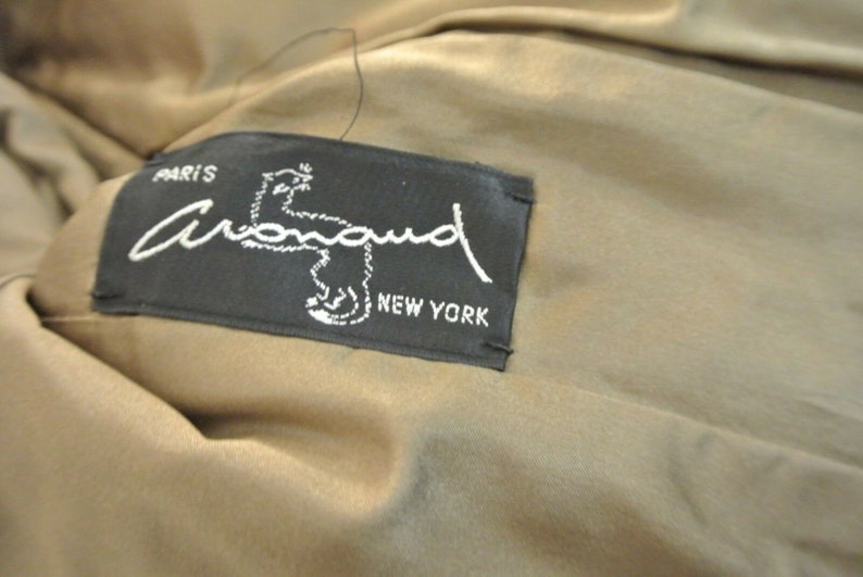 K&ouml;nnte beinhalten: Ein schwarz-wei&szlig;es Etikett mit dem Text "Paris Armand New York" und einem stilisierten Bild eines kleinen Tieres.
