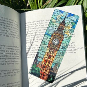 May include: A rectangular bookmark featuring a stained-glass design of the Elizabeth Tower, also known as Big Ben. The bookmark is placed on an open book with text visible. The bookmark is approximately 2 inches wide and 6 inches long.