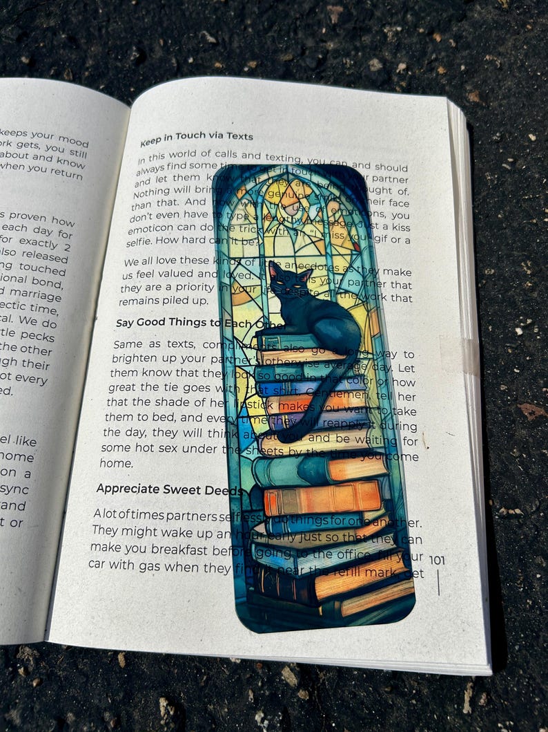 Puede incluir: Un marcap&aacute;ginas rectangular con un gato negro sobre una pila de libros, con un dise&ntilde;o de vidriera. El texto "Keep in Touch via Texts" es visible en la parte superior del marcap&aacute;ginas.