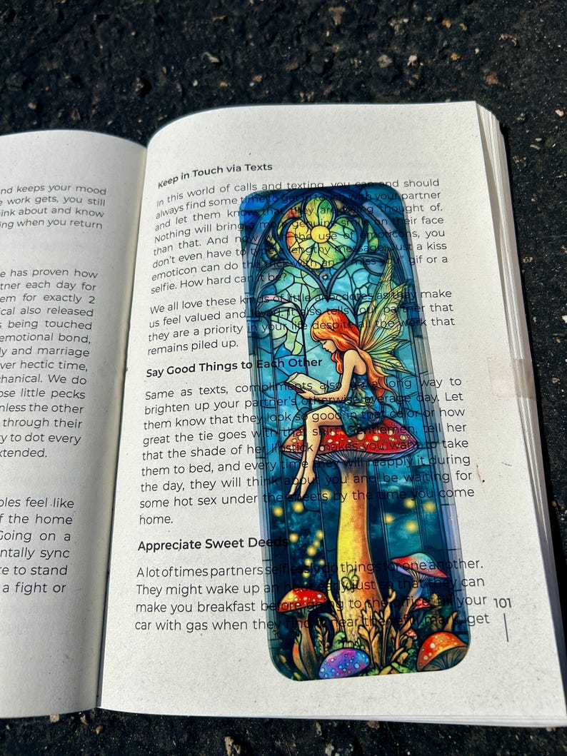 May include: A rectangular sticker featuring a fairy with red hair sitting on a mushroom. The fairy is reading a book, and the background is a stained-glass window design with colorful mushrooms.