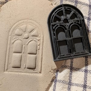 May include: A black plastic window mold for making impressions in clay or dough. The mold is shaped like a double-hung window with a decorative arched top and a grid pattern.
