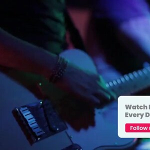 May include: A white electric guitar is held by a person, with the neck and strings visible. The image is bathed in blue and red stage lighting. A small white box with the text "Watch New Videos Every Day" and "Follow me" is in the lower right corner.