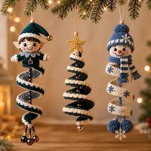 Puede incluir: Tres adornos de ganchillo colgantes: un elfo verde azulado con cola en espiral y cascabeles, un árbol de Navidad en espiral verde y blanco con una estrella amarilla, y un muñeco de nieve azul y blanco con cuerpo en espiral, bufanda y copos.