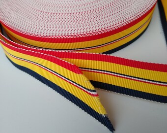 Puede incluir: Un rollo de cinta de rayas amarillas, rojas y azul marino con detalles blancos. La cinta es 100% acetato y lavable. La etiqueta en el rollo dice "100% ACETATO LAVABLE 30 DEG. PRESS 80 DEG."