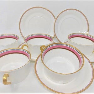 May include: Set of six white teacups and saucers with gold trim and pink and blue stripes.