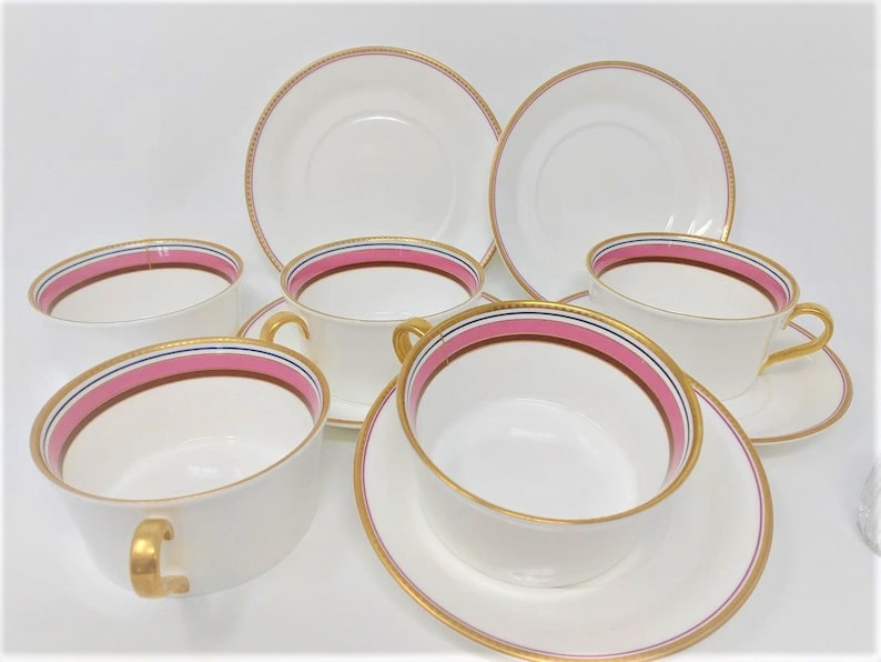 May include: Set of six white teacups and saucers with gold trim and pink and blue stripes.