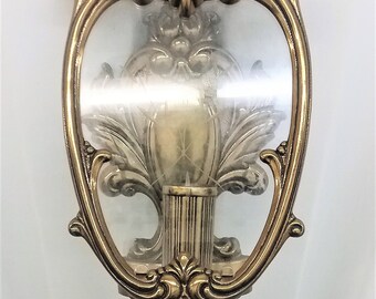 May include: A gold-toned wall sconce with a glass shade and ornate detailing. The sconce has a floral design and a fluted column.