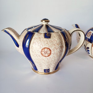 May include: A white teapot with blue and gold accents. The teapot has a floral design and a round body.