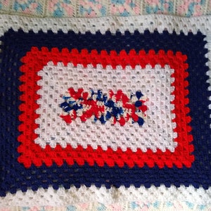 May include: A white crocheted blanket with a red, white, and blue border. The center of the blanket features a red, white, and blue crocheted design.