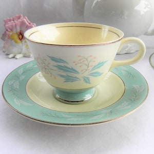 May include: A vintage teacup and saucer set with a delicate floral design. The cup and saucer are white with a light blue and pink floral pattern. The cup has a gold rim and the saucer has a gold trim.