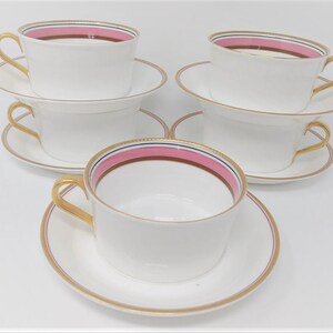 May include: Set of four white teacups and saucers with gold trim and a pink and brown stripe design.