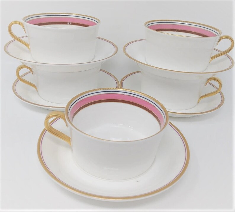 May include: Set of four white teacups and saucers with gold trim and a pink and brown stripe design.