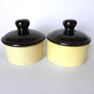 May include: Two ceramic jars with lids. The jars are yellow with brown lids. The lids have a rounded knob on top.