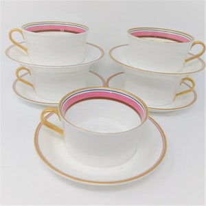 May include: Set of four white teacups and saucers with gold trim and a pink and blue stripe around the rim.