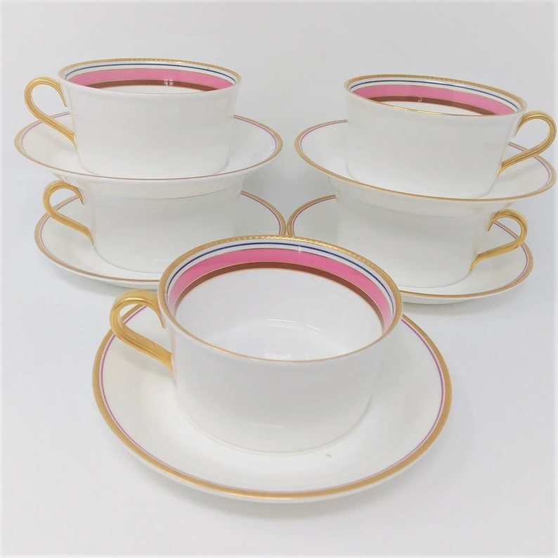 May include: Set of four white teacups and saucers with gold trim and a pink and blue stripe around the rim.