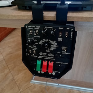May include: Black control panel with various switches, dials, and labels, including "RANGE MG BURST" and "ROCKET BOMB." The panel is mounted with black brackets. The text "LAUNCHER ARMED" is visible.