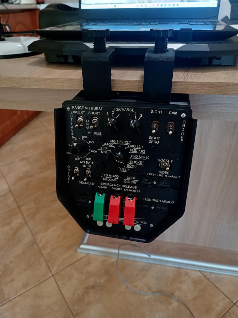 May include: Black control panel with various switches, dials, and labels, including "RANGE MG BURST" and "ROCKET BOMB." The panel is mounted with black brackets. The text "LAUNCHER ARMED" is visible.