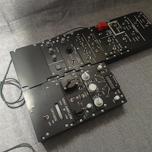 May include: Black control panel with numerous switches, dials, and buttons. The panel includes labels such as "Vent Airflow" and "Oxygen." A red switch is visible. A digital display shows numbers. A black and grey cord is connected to the panel.