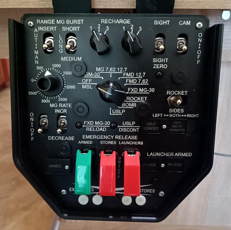 May include: A black control panel with various switches, dials, and labels. Features include "RANGE MG BURST," "RECHARGE," and "ROCKET." The panel has green and red switches labeled "ARMED" and "STORES."