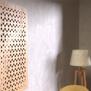 Puede incluir: Un panel acústico de madera marrón claro con un patrón circular de agujeros. El panel está montado en una pared blanca.