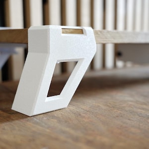 May include: A low-angle shot of a small, modern wooden table with white, geometric legs. The tabletop is a light brown, and the legs are a textured white. The table is on a wooden surface.