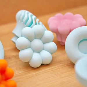 Peut inclure: Une collection d'objets décoratifs aux couleurs pastel, dont un élément en forme de fleur bleu clair, une fleur rose et un bouton. Les objets sont disposés sur une surface en bois, créant une esthétique douce et invitante.