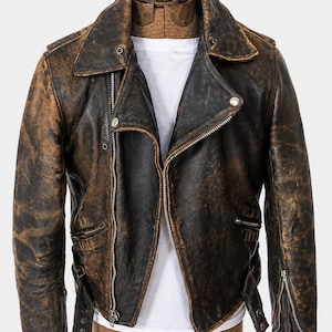 Puede incluir: Una chaqueta de moto de cuero marrón oscuro desgastado con cremallera metálica asimétrica plateada, cuello ancho con botones a presión, puños con cremallera y cinturón, sobre una camiseta blanca lisa en un torso de maniquí.
