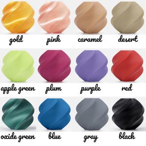 May include: A collection of twelve decorative, spiral-shaped objects in various colors, including gold, pink, caramel, desert, apple green, plum, purple, red, oxide green, blue, gray, and black. Each object has a smooth, curved design with the color name written below.
