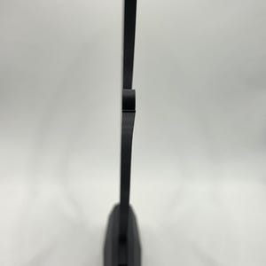 May include: A black, geometric-shaped object with a flat base and a vertical, rectangular extension. The object is made of a solid, opaque material and stands against a white background. The design is minimalist and modern.