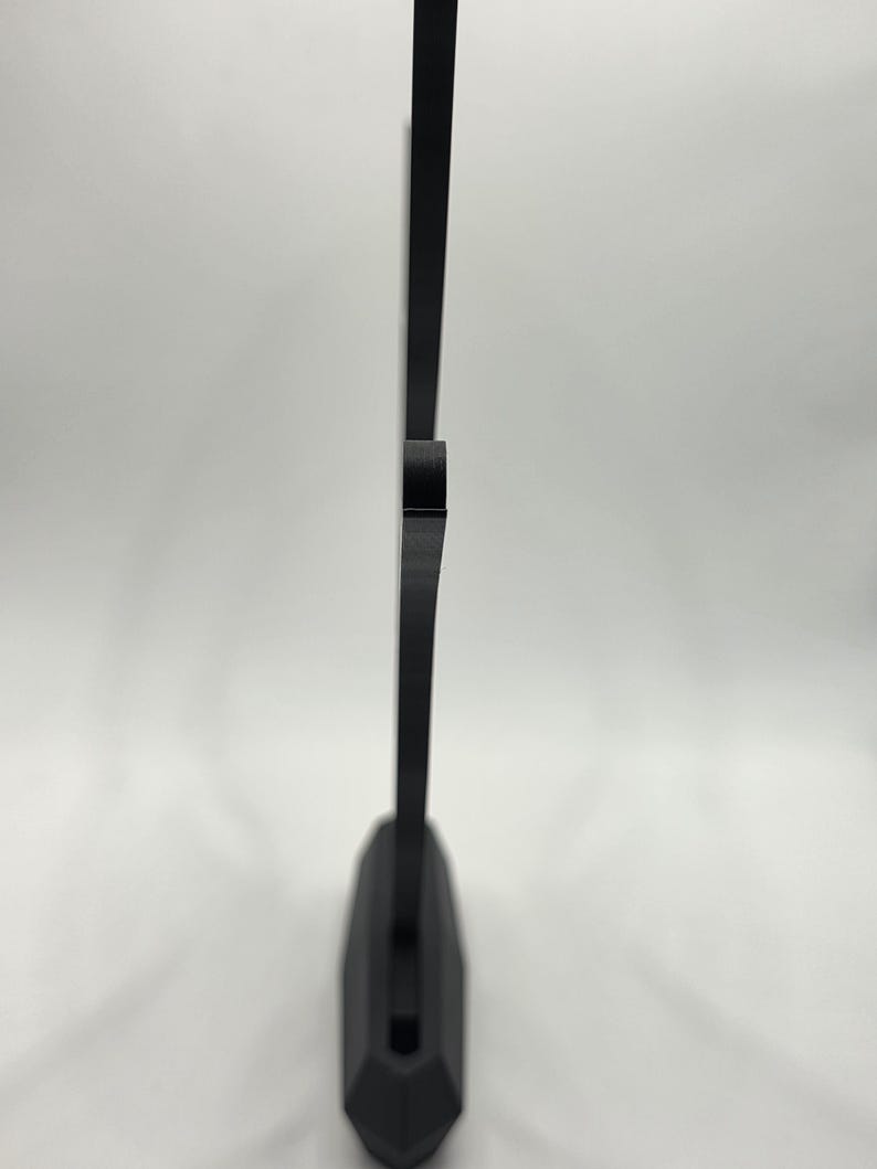 May include: A black, geometric-shaped object with a flat base and a vertical, rectangular extension. The object is made of a solid, opaque material and stands against a white background. The design is minimalist and modern.