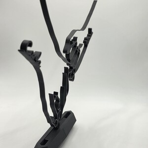 May include: A black, abstract metal sculpture with a geometric base and flowing, linear elements. The sculpture has a modern design, with curved and angular shapes. The piece is set against a white background, highlighting its form.