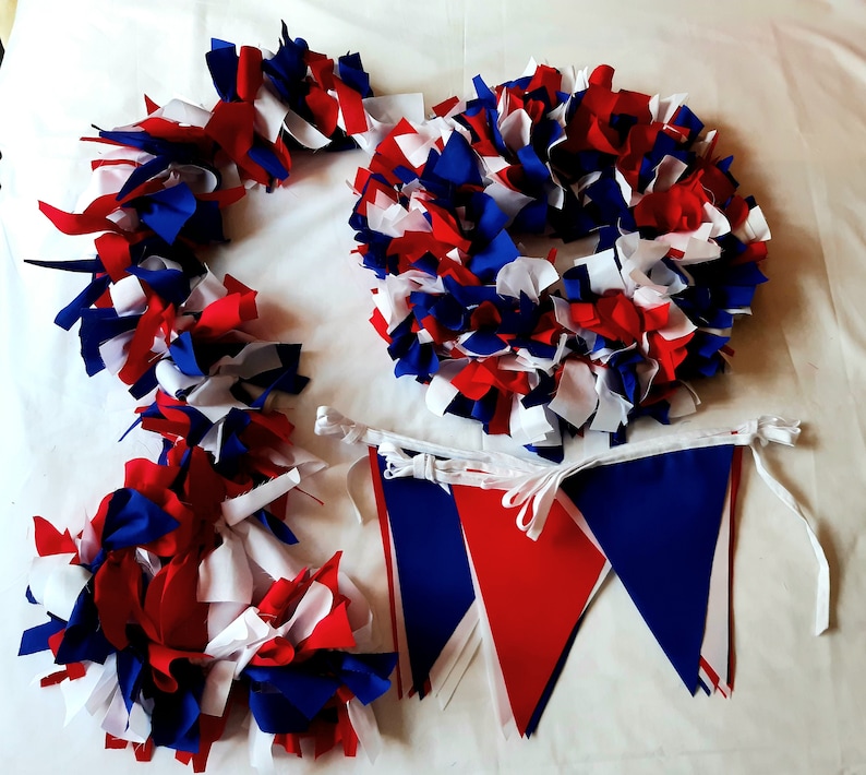 May include: A patriotic collection of red, white, and blue fabric decorations. The image features a wreath, garland, and bunting. The wreath and garland are made of fabric strips. The bunting has red and blue triangular flags.